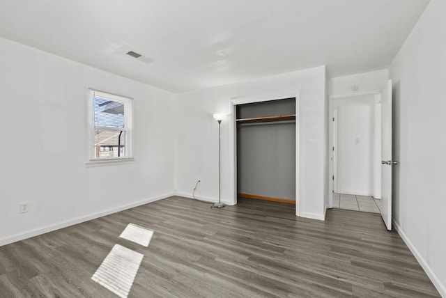 unfurnished bedroom featuring a closet, wood finished floors, visible vents, and baseboards