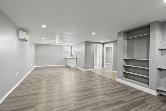 basement featuring baseboards, a wall mounted AC, wood finished floors, and recessed lighting