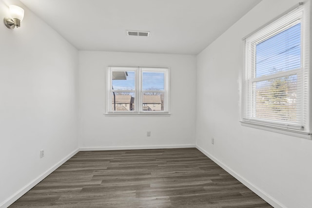 empty room featuring baseboards, visible vents, dark wood finished floors, and a wealth of natural light