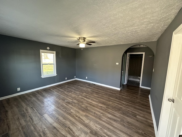 spare room with arched walkways, a textured ceiling, dark wood-style flooring, a ceiling fan, and baseboards