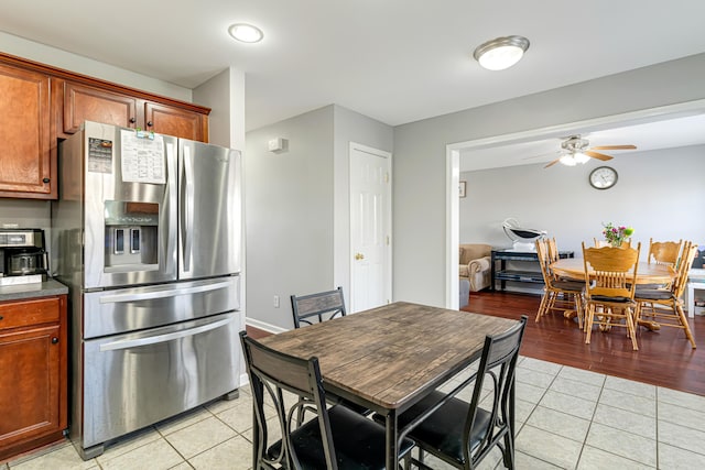 kitchen featuring light tile patterned floors, dark countertops, ceiling fan, brown cabinets, and stainless steel refrigerator with ice dispenser