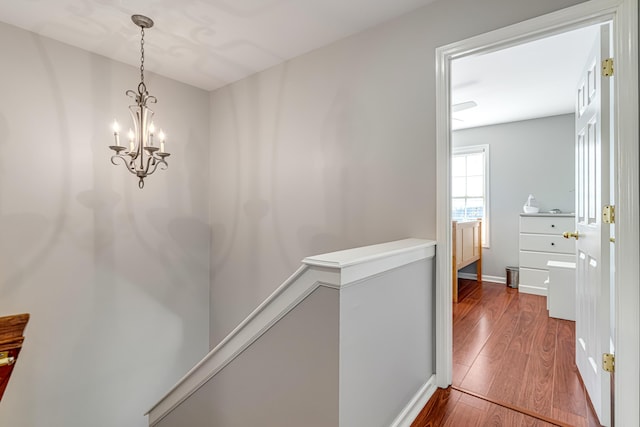 hallway featuring an inviting chandelier, baseboards, wood finished floors, and an upstairs landing