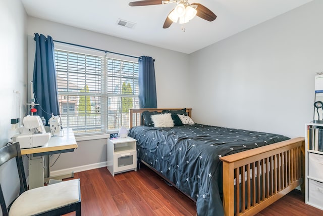 bedroom with a ceiling fan, visible vents, baseboards, and wood finished floors