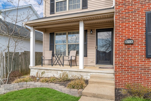 property entrance featuring a porch, brick siding, and fence