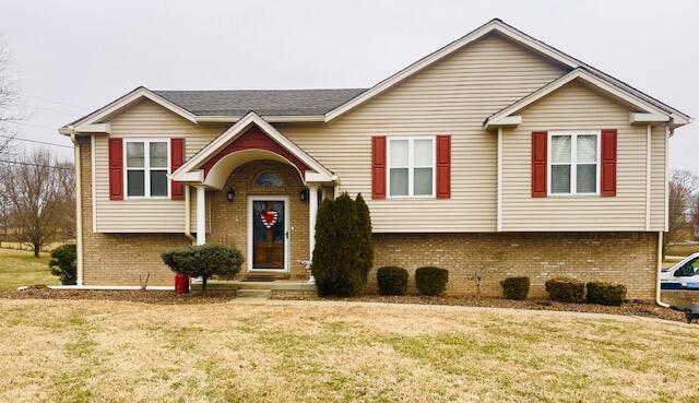 raised ranch featuring brick siding and a front yard