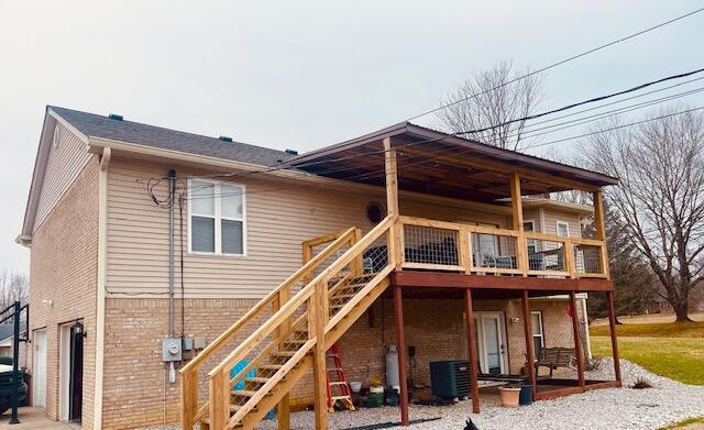 back of house with brick siding, driveway, central AC, and stairs