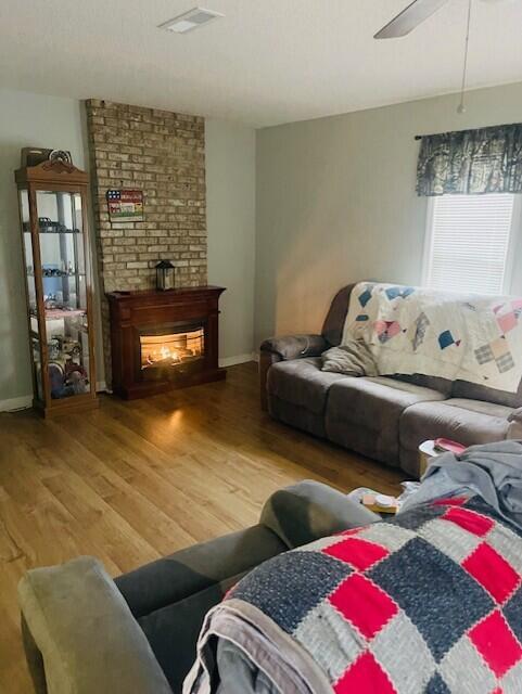 living room with ceiling fan, a fireplace, wood finished floors, visible vents, and baseboards