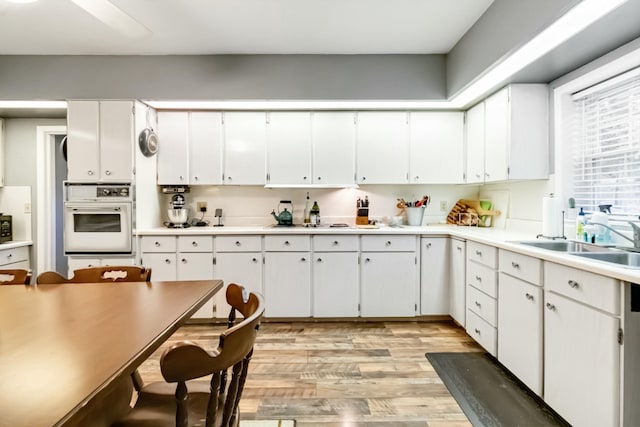 kitchen featuring white oven, light countertops, light wood-style flooring, white cabinets, and a sink