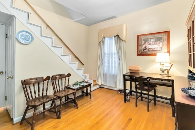 living area featuring a baseboard heating unit, light wood-type flooring, baseboards, and stairs