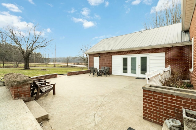 exterior space with french doors, brick siding, metal roof, and a patio