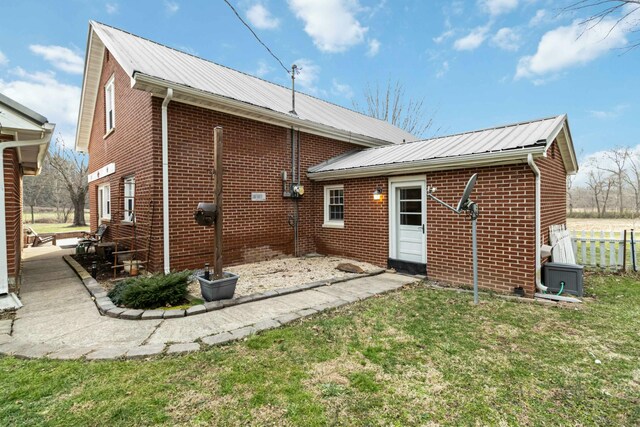 back of property with a yard, metal roof, brick siding, and fence