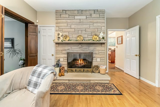 living area featuring a stone fireplace, wood finished floors, and baseboards