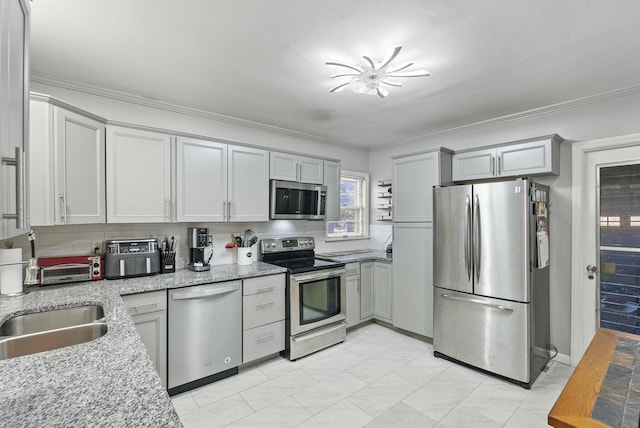 kitchen featuring light stone counters, crown molding, backsplash, gray cabinetry, and appliances with stainless steel finishes