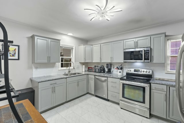 kitchen with appliances with stainless steel finishes, gray cabinets, a sink, and light stone counters