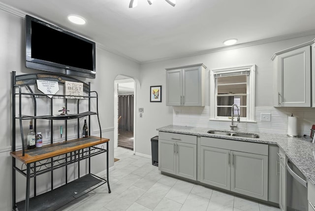 kitchen featuring arched walkways, tasteful backsplash, stainless steel dishwasher, gray cabinetry, and a sink