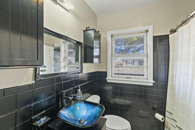 full bath featuring toilet, a wainscoted wall, a sink, tile walls, and a shower with curtain