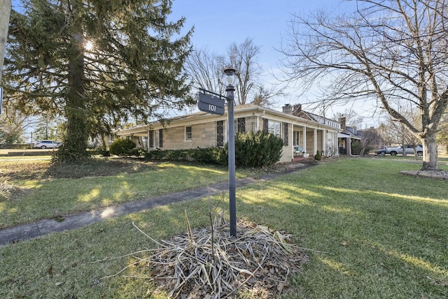 view of side of home with stone siding, a yard, and a chimney