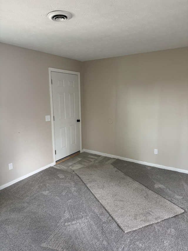 spare room featuring a textured ceiling, carpet, visible vents, and baseboards