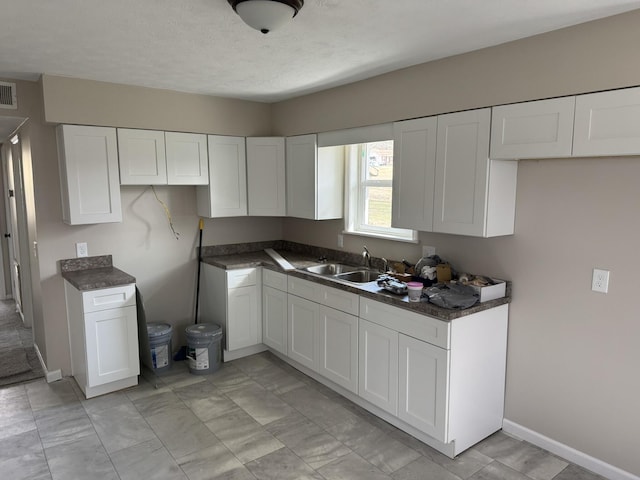 kitchen with baseboards, visible vents, dark countertops, white cabinetry, and a sink