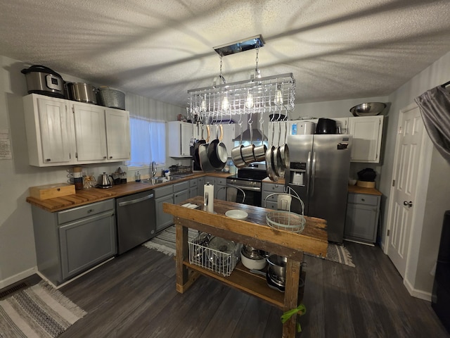 kitchen with stainless steel appliances, butcher block countertops, a sink, and white cabinetry