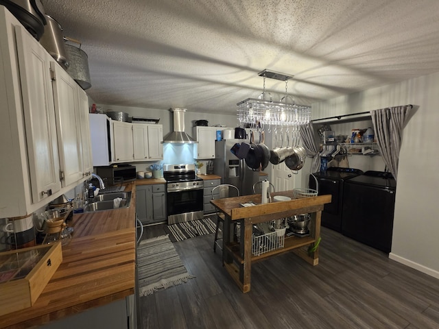 kitchen with appliances with stainless steel finishes, washing machine and dryer, a sink, wood counters, and wall chimney range hood