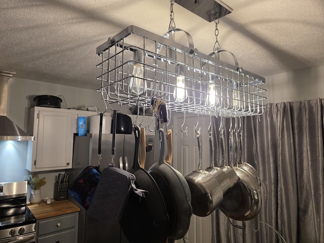 interior space featuring a textured ceiling, wall chimney exhaust hood, and stainless steel range with electric cooktop