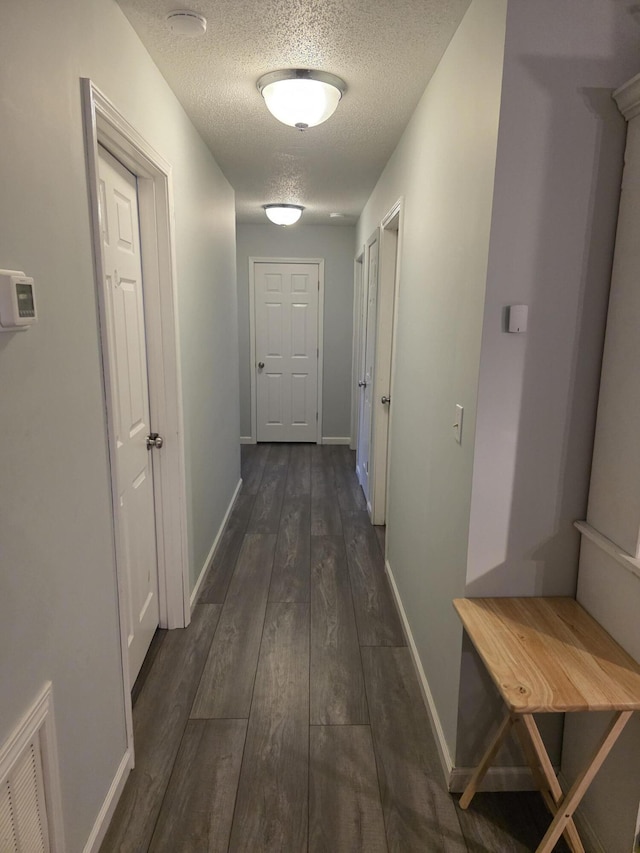 corridor with visible vents, dark wood finished floors, a textured ceiling, and baseboards