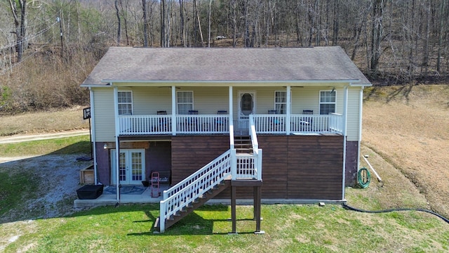 view of front of house with french doors, a shingled roof, covered porch, stairway, and a front lawn