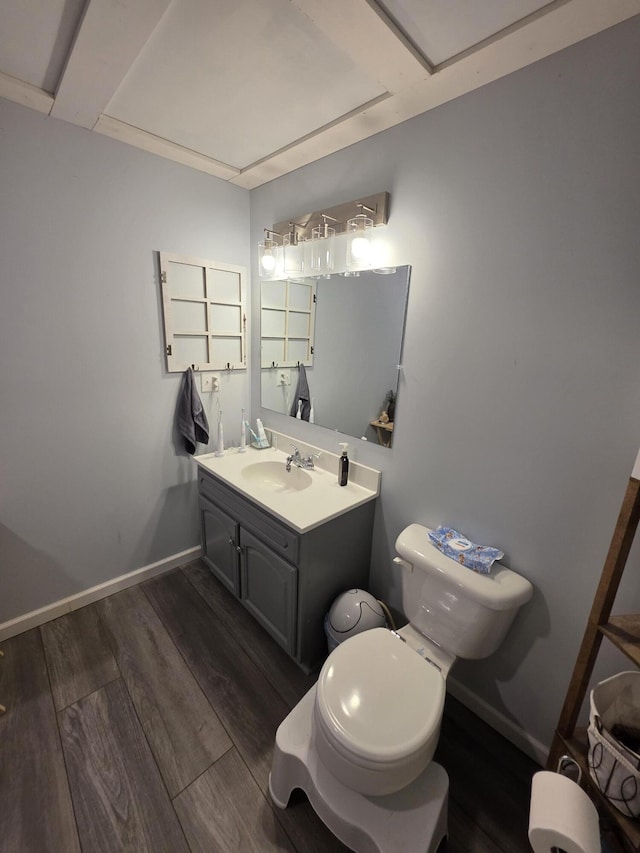 half bath featuring toilet, vanity, baseboards, and wood finished floors