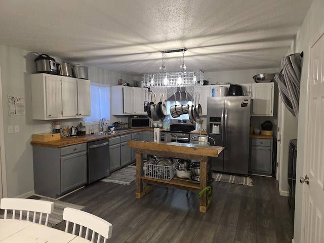 kitchen featuring dark wood finished floors, appliances with stainless steel finishes, a textured ceiling, wooden counters, and a sink