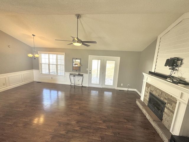 unfurnished living room featuring vaulted ceiling, a fireplace with raised hearth, a textured ceiling, and dark wood-style floors