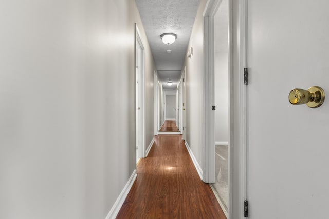 hall featuring baseboards, a textured ceiling, and wood finished floors