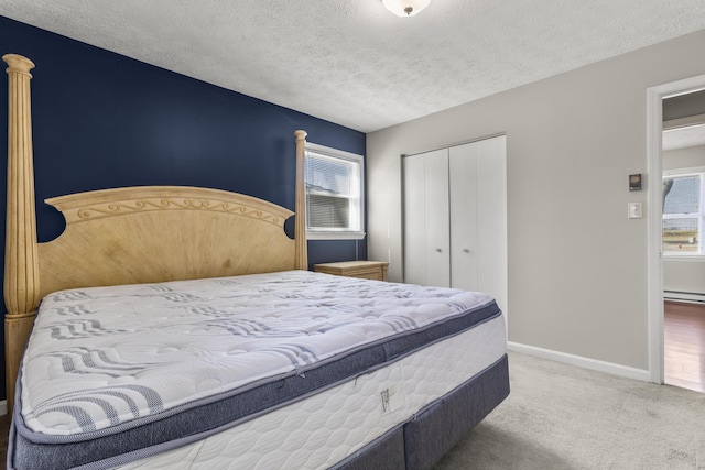 carpeted bedroom with a baseboard radiator, baseboards, a closet, and a textured ceiling