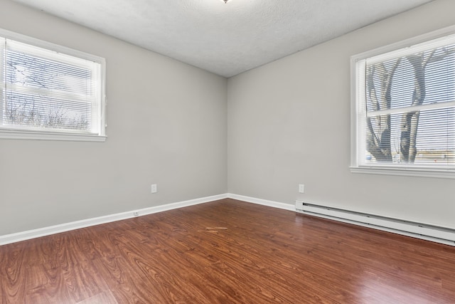 unfurnished room with dark wood-style floors, a textured ceiling, a baseboard heating unit, and baseboards