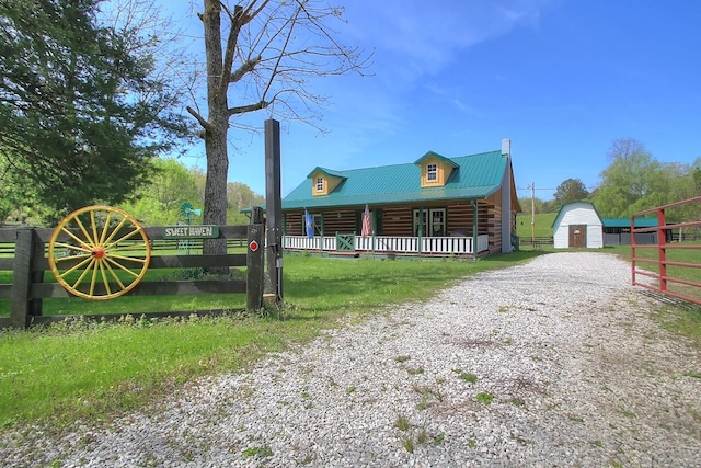 view of front facade featuring covered porch, metal roof, gravel driveway, and an outdoor structure