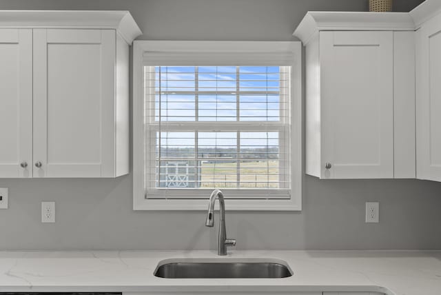 kitchen with light stone countertops, white cabinetry, and a sink