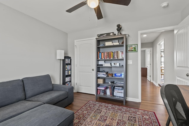 living area featuring dark wood-type flooring, ceiling fan, and baseboards