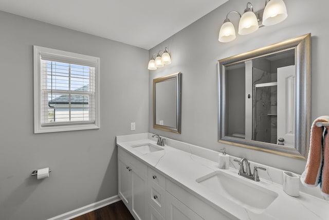 bathroom featuring double vanity, a sink, a shower with door, and baseboards