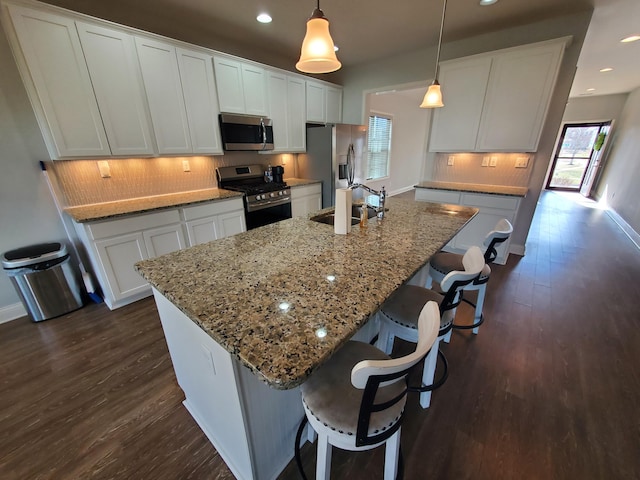 kitchen featuring tasteful backsplash, appliances with stainless steel finishes, dark wood-type flooring, a kitchen island with sink, and a sink