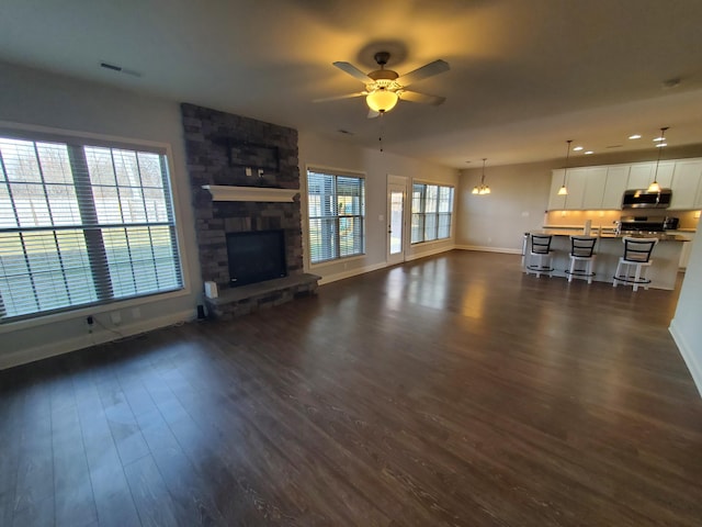 unfurnished living room featuring ceiling fan, dark wood-style flooring, a fireplace, visible vents, and baseboards