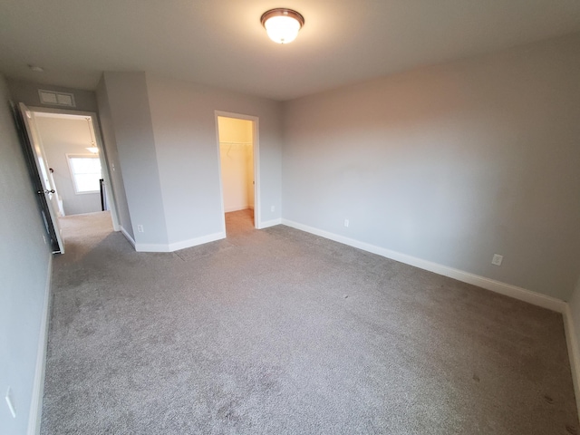 unfurnished bedroom featuring carpet, a walk in closet, a closet, visible vents, and baseboards