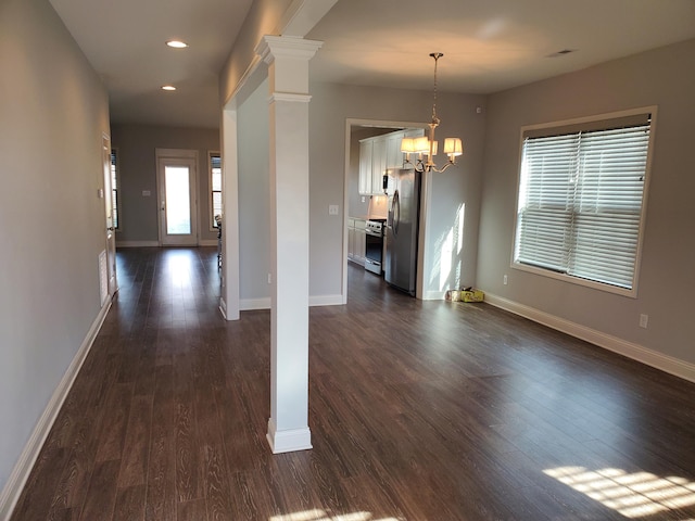 unfurnished dining area with a chandelier, dark wood-style flooring, and decorative columns