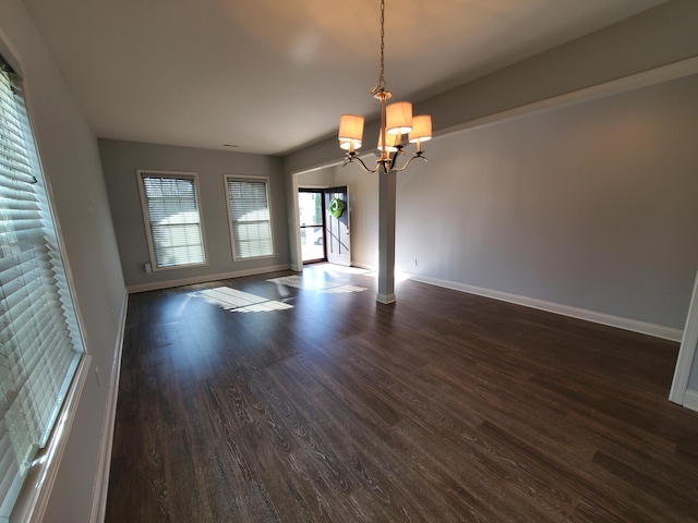 unfurnished dining area with dark wood-style flooring, a notable chandelier, baseboards, and ornate columns