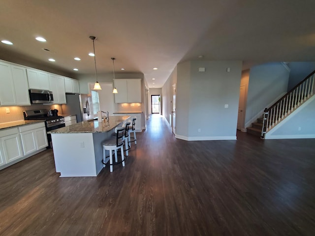 kitchen featuring a kitchen island with sink, stainless steel appliances, a breakfast bar, dark wood-style flooring, and dark stone counters