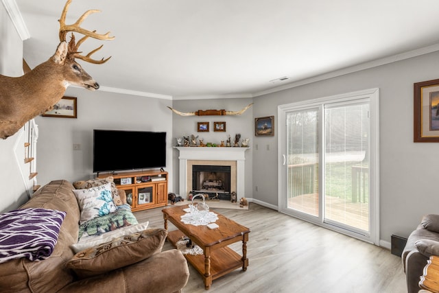 living room with crown molding, a fireplace, visible vents, light wood-type flooring, and baseboards