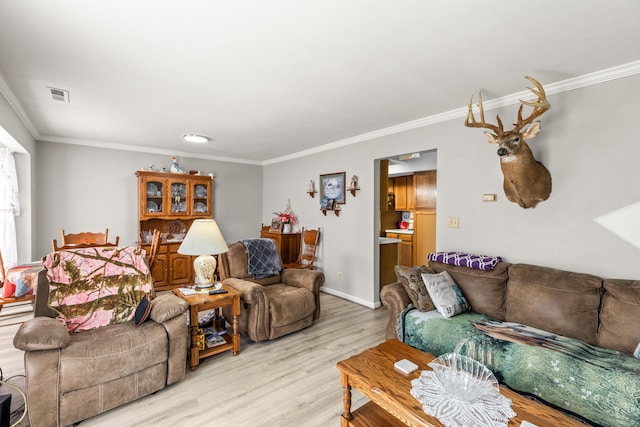 living room with ornamental molding, light wood-type flooring, visible vents, and baseboards