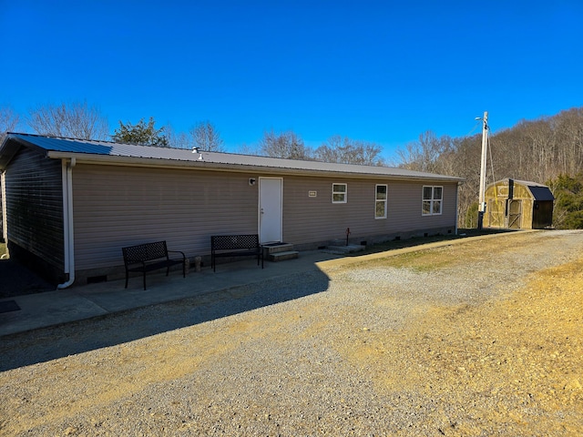 back of property with entry steps, metal roof, a patio, and an outbuilding