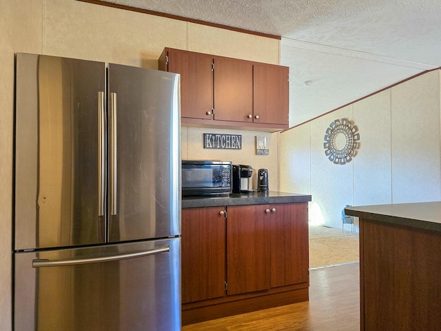 kitchen featuring black microwave, a textured ceiling, wood finished floors, freestanding refrigerator, and dark countertops