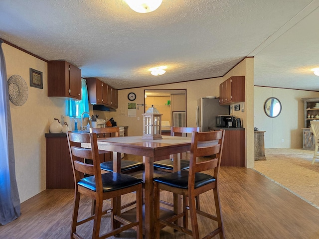 dining area with ornamental molding, lofted ceiling, a textured ceiling, and wood finished floors