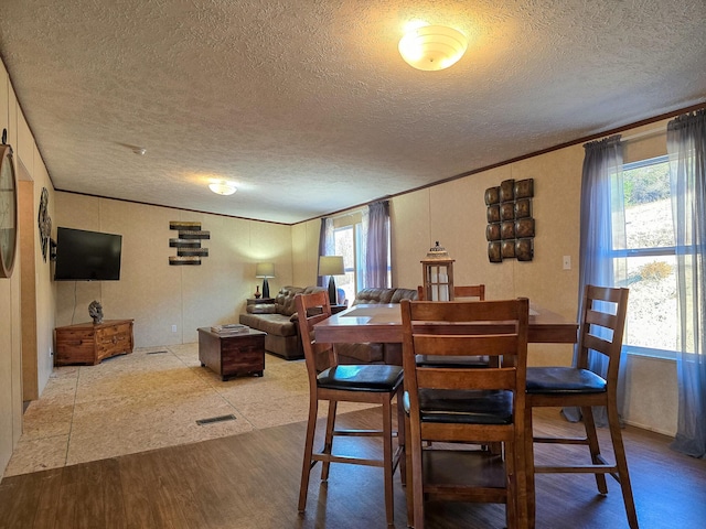 dining space featuring a textured ceiling, ornamental molding, plenty of natural light, and wood finished floors